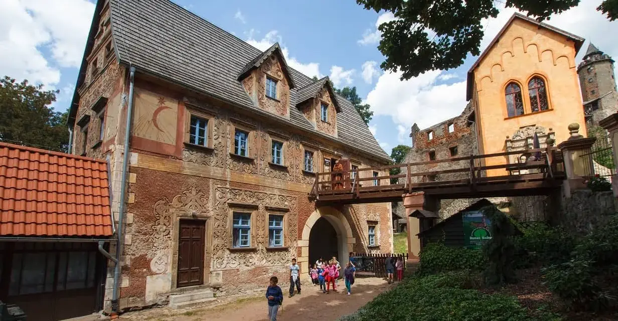 Zamek Książ i jego okolice to jedne z najpiękniejszych wałbrzych atrakcje. Drewniany most łączy zabytkowe budynki, a dzieci zwiedzają teren.