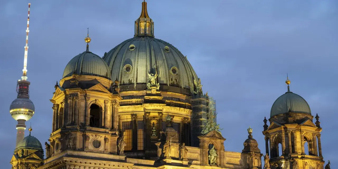 Prachtvolle Kuppeln des Berliner Doms im Abendlicht, mit dem Fernsehturm im Hintergrund. Ein Wahrzeichen der Kirchen in Berlin.