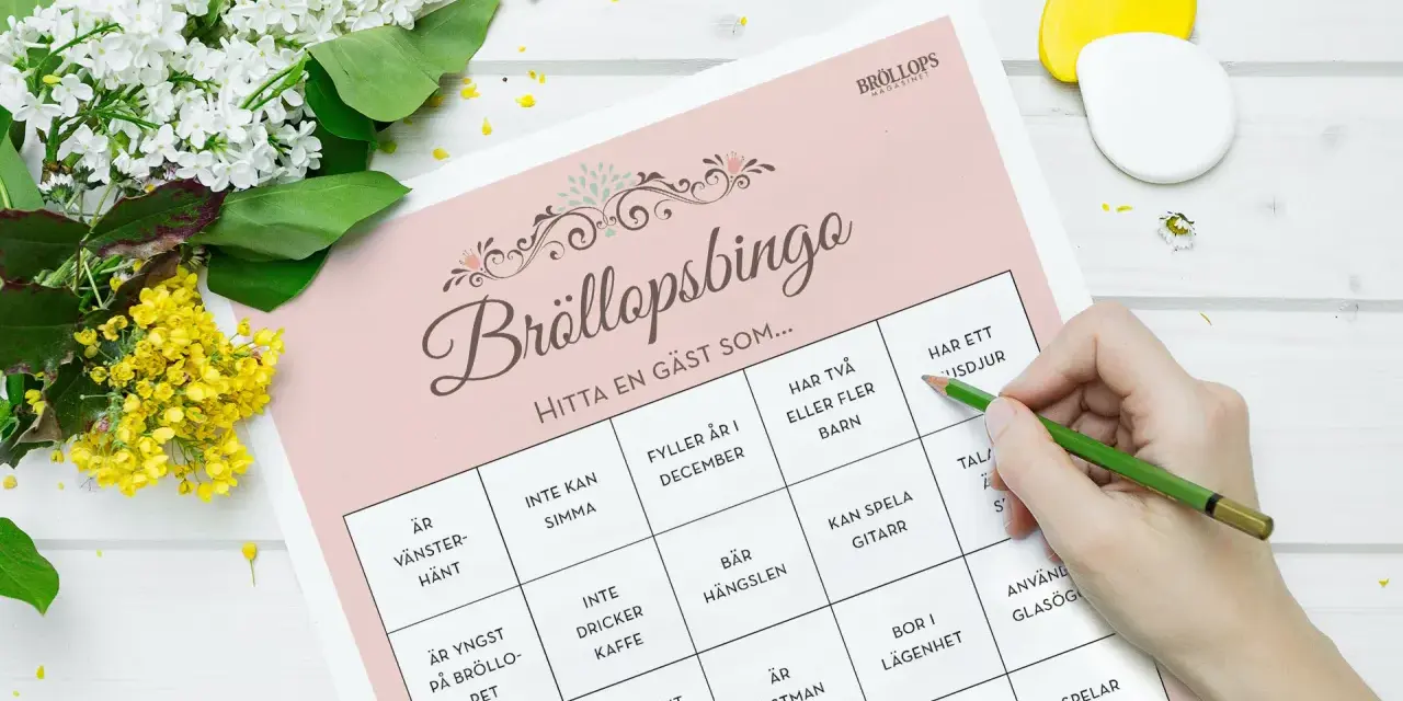 Bröllopsbingo med roliga frågor med svar. En hand med en grön penna markerar rutor på ett spelblad. Blommor ligger bredvid.