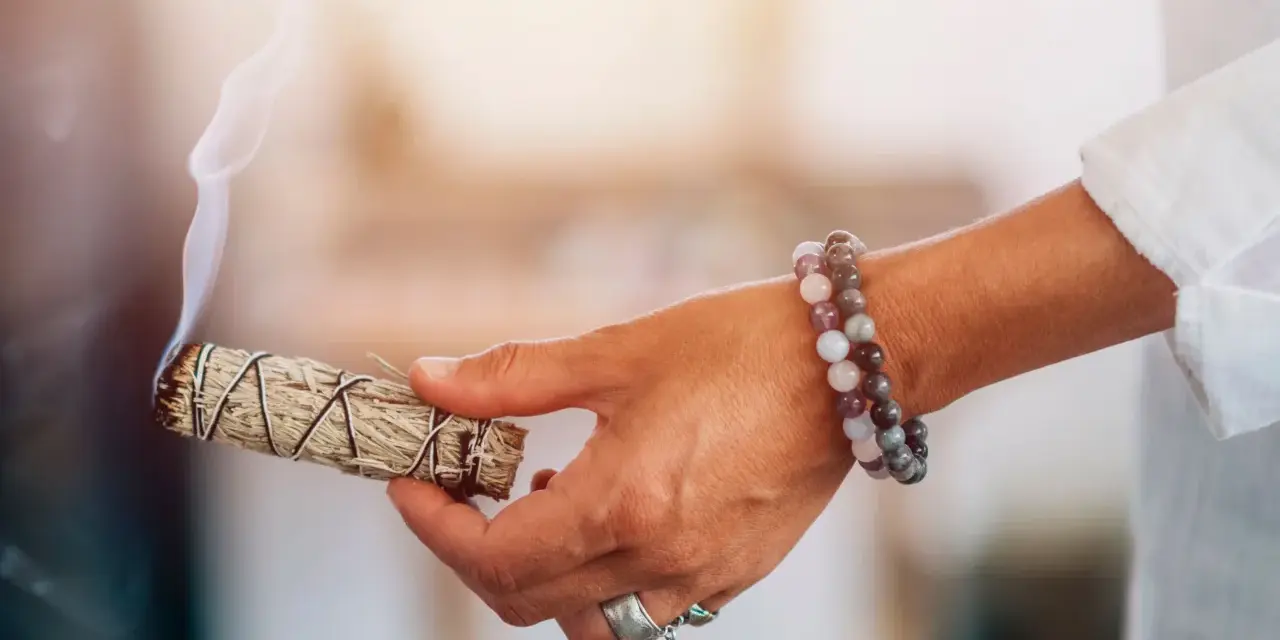 Mano con un manojo de salvia humeante, lista para sahumar la casa y purificar el ambiente.