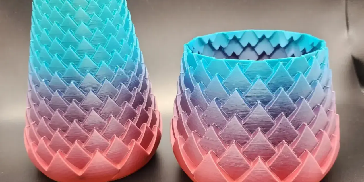 Two dragon-scale patterned vases, created with color 3d printing, showcase a gradient from coral pink to teal blue.