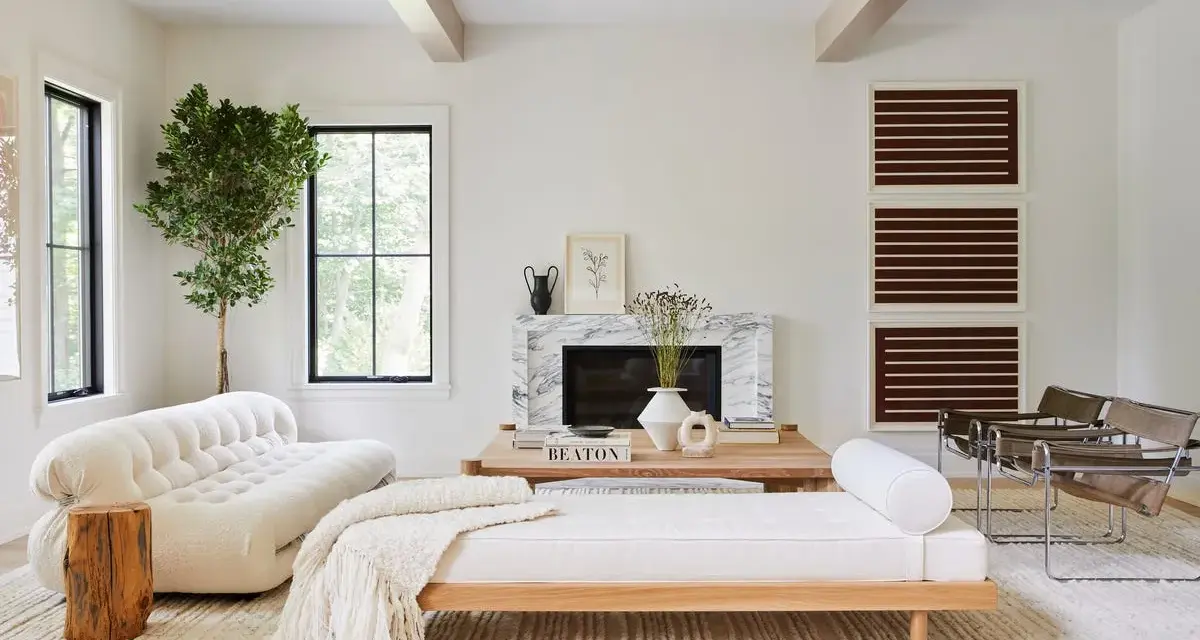 Elegante salón con decoración blanco y madera natural. Sofá curvo blanco, diván de madera, chimenea de mármol y plantas.
