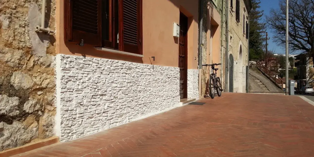 Una parete umida è stata rivestita con pietre bianche, migliorando l'estetica e la protezione dell'edificio.