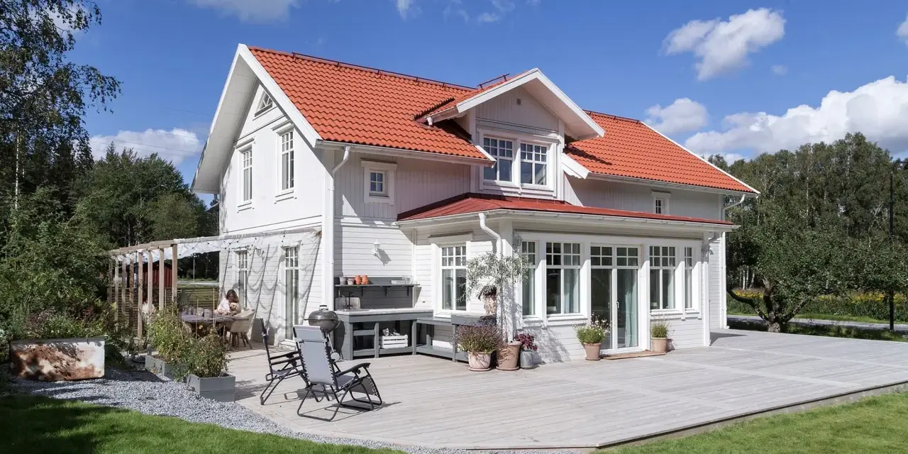 Vitt hus med rött tak och stor altan. Perfekt för att behandla altan och njuta av sommaren.