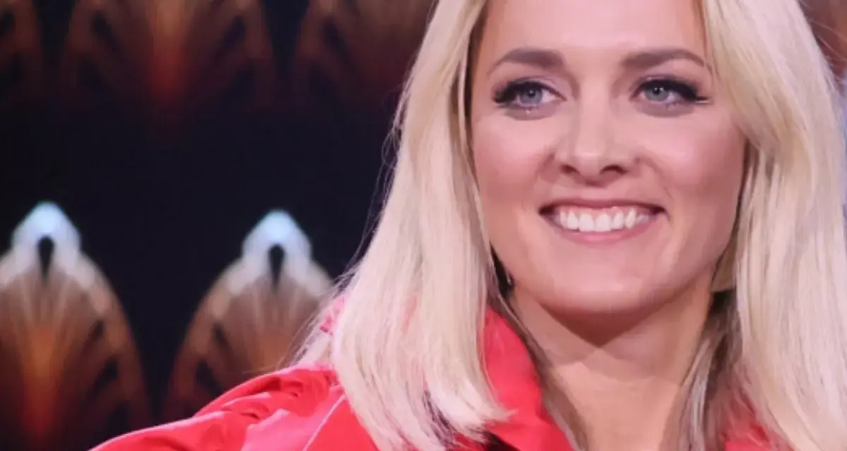 Uśmiechnięta blondynka w czerwonej marynarce, z błękitnymi oczami i delikatnym naszyjnikiem. Ola, jaka to melodia?