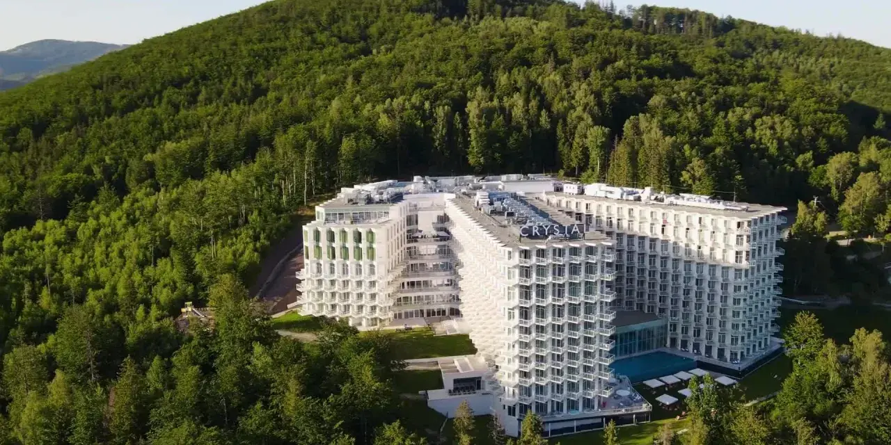 Nowy hotel w Wiśle, Crystal Mountain, wtopiony w zielone zbocze góry. Nowoczesna architektura z licznymi balkonami i basenem.