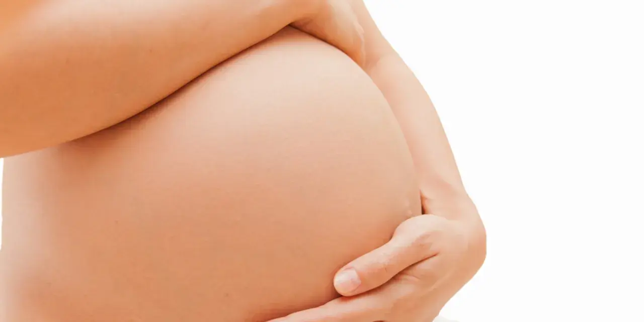 Dłoń obejmuje ciążowy brzuch. Zaparcia w ciąży to częsty problem, ale można sobie z nimi radzić.