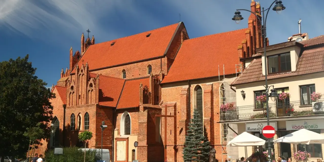 Gotycka ceglana bazylika w Tczewie, z pomarańczowym dachem, to jedna z głównych atrakcji miasta. W tle kawiarniany ogródek.