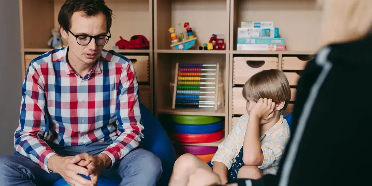 Terapeuta rozmawia z dzieckiem, ćwicząc teorię umysłu. W tle zabawki i pomoce edukacyjne.