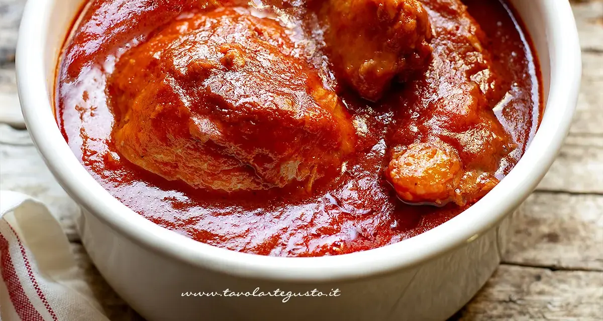 Un saporito ragù napoletano in una ciotola bianca, con pezzi di carne succulenta immersi nel sugo rosso intenso.