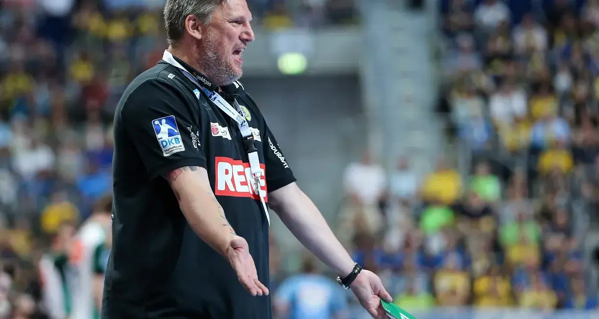 Trener Nikolaj Jacobsen w czarnej koszulce z logo DKB, gestykuluje na tle trybun pełnych kibiców.