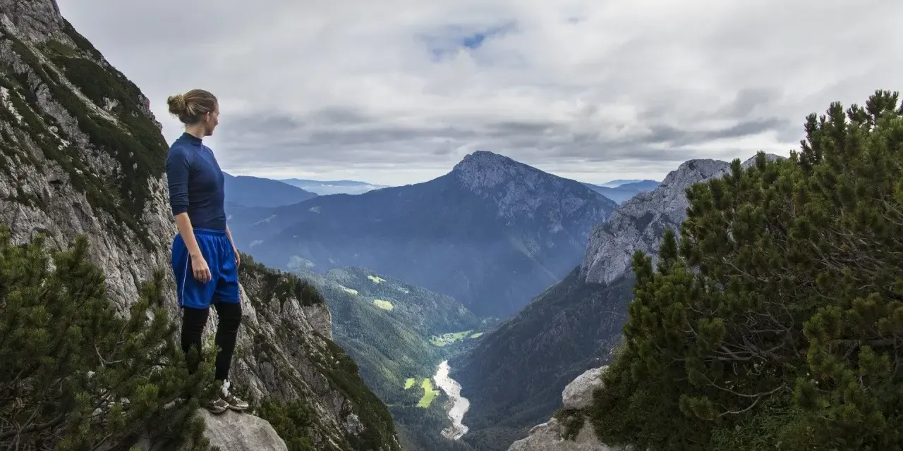 Donna in cima a una montagna, contemplando un vasto paesaggio alpino. Il vero hiking significato è nella libertà e nella vista mozzafiato.