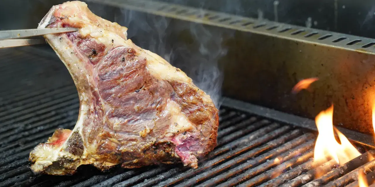 Una succulenta bistecca alla fiorentina, con la sua storia di sapori, cuoce sulla griglia tra fiamme vive e fumo.