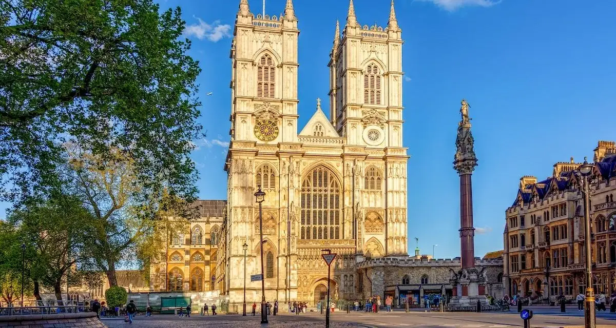 L'abbaye de Westminster, majestueuse et illuminée par le soleil, se dresse fièrement avec ses tours jumelles. Une colonne commémorative se dresse à droite.