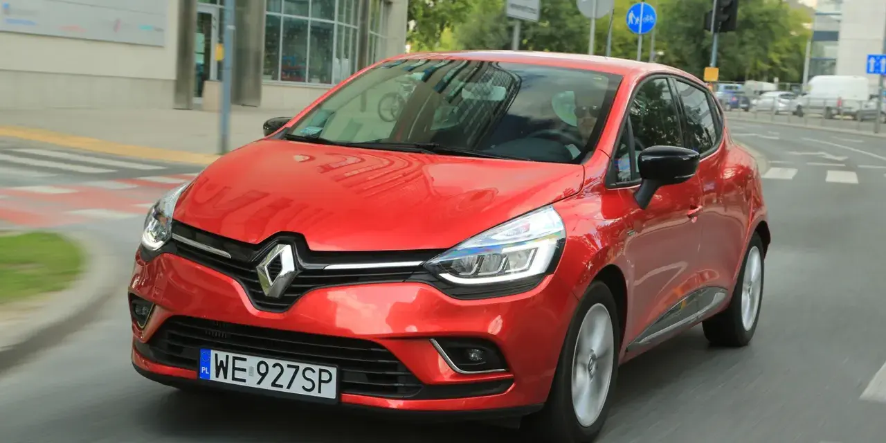 Czerwony Renault Clio 3 1.2 benzyna w ruchu miejskim. Kierowca w okularach przeciwsłonecznych.