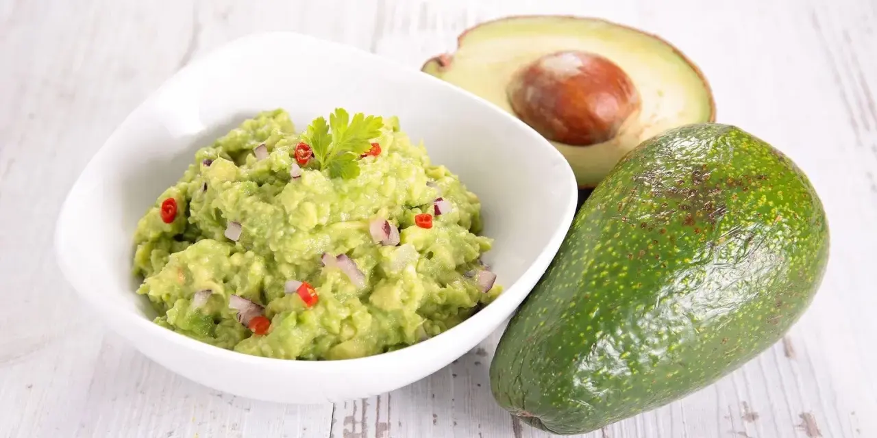 Miseczka guacamole z awokado, cebulą i papryczką chili na drewnianym tle.