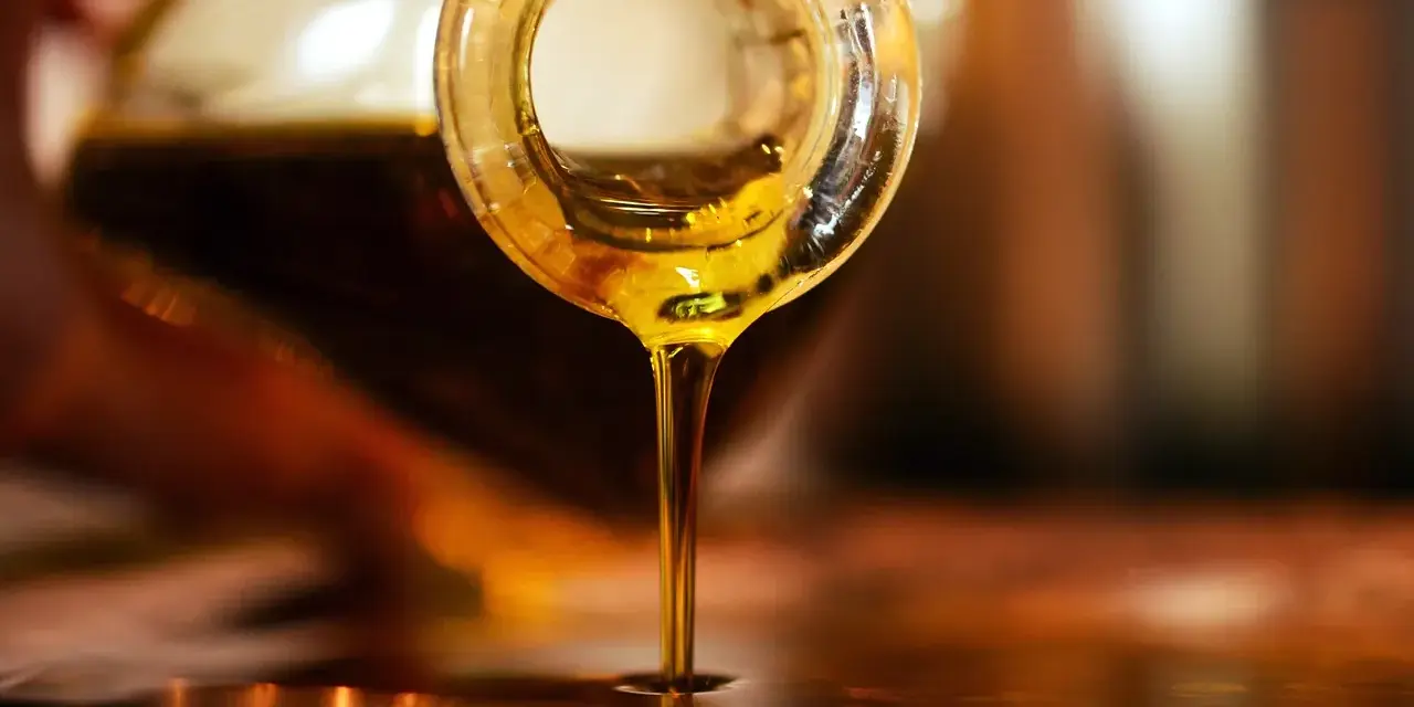 Olio d'oliva dorato cola da una bottiglia. Scopri come conservare l'olio di oliva per mantenerne intatto il sapore.
