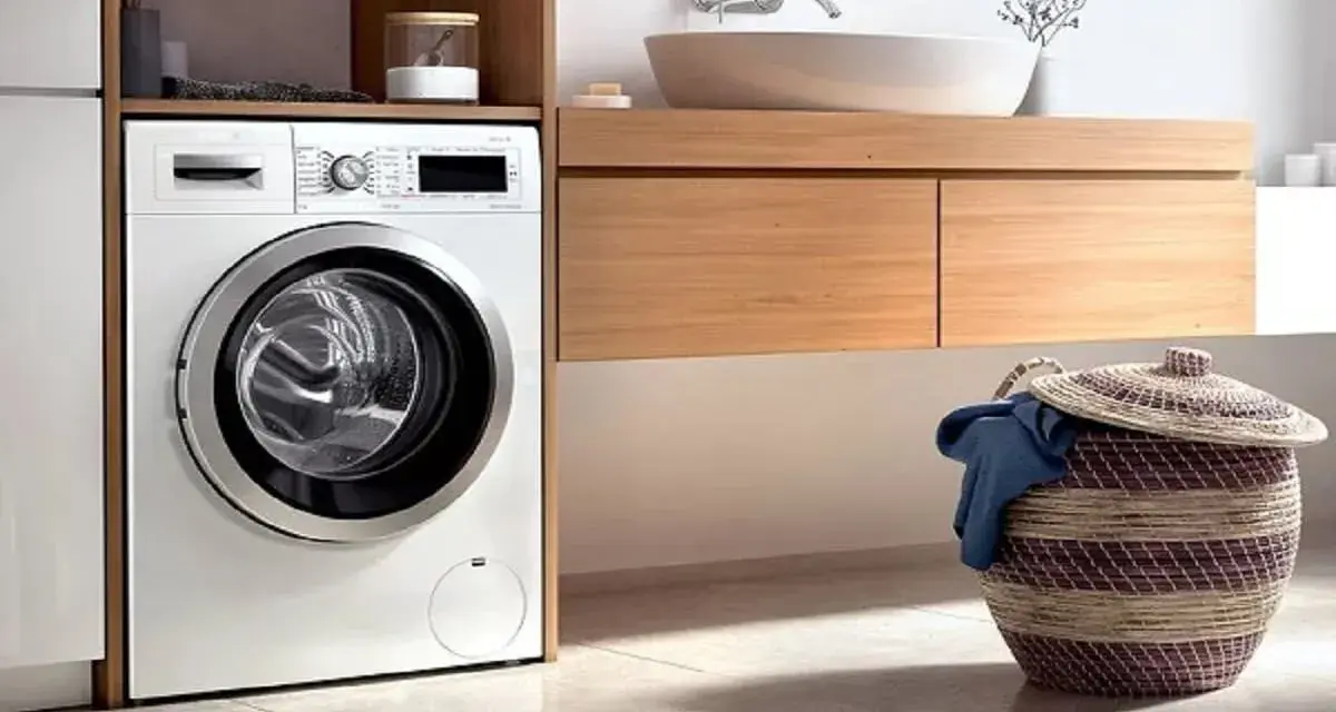 Lavadora blanca moderna lista para instalar en un baño con cesta de ropa sucia.