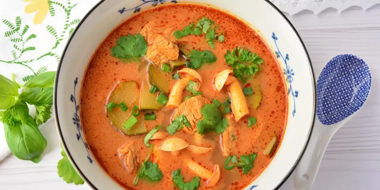 Aksamitny tom yum z kurczakiem, grzybami i kolendrą w misce z niebieskim wzorem. Obok leży łyżka.