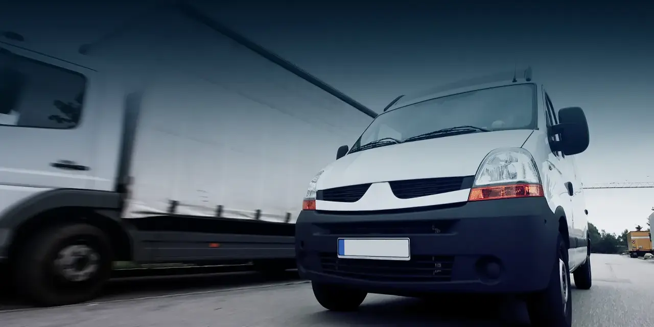Biały bus i ciężarówka w ruchu drogowym. To obraz idealny dla osób, które chcą rozpocząć pracę z własnym busem i rozwijać swoją firmę transportową.