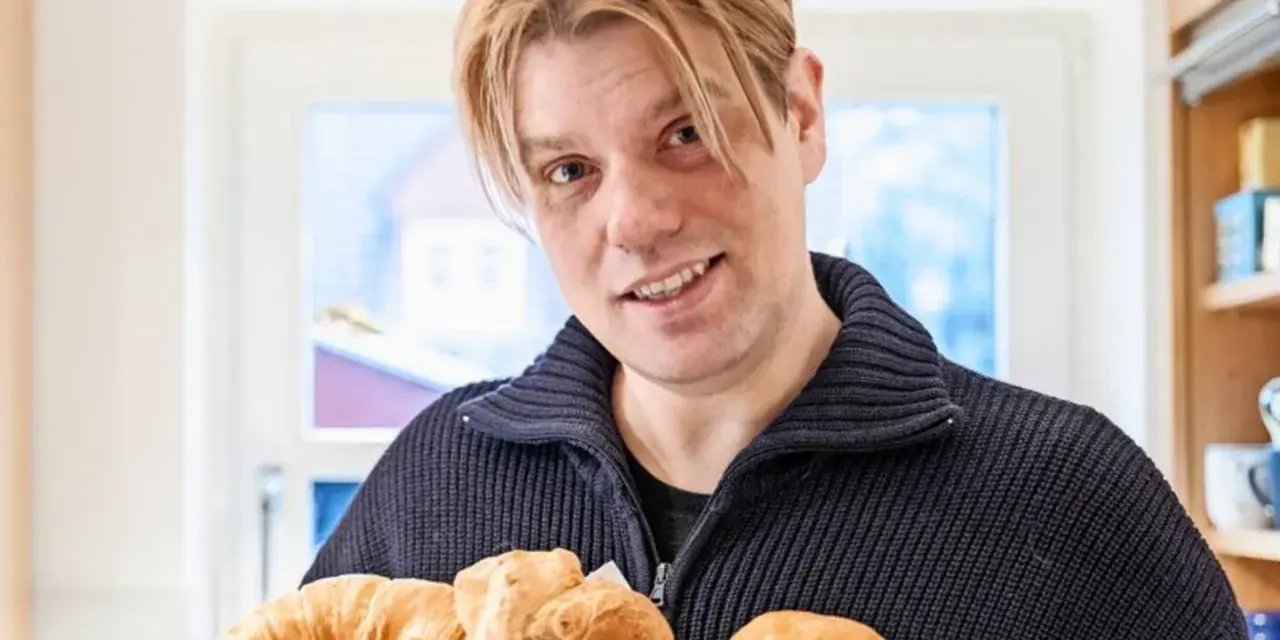 Mann mit blonden Haaren hält einen Korb mit frischen Backwaren, darunter ein Croissant und ein Kieler Semmel.