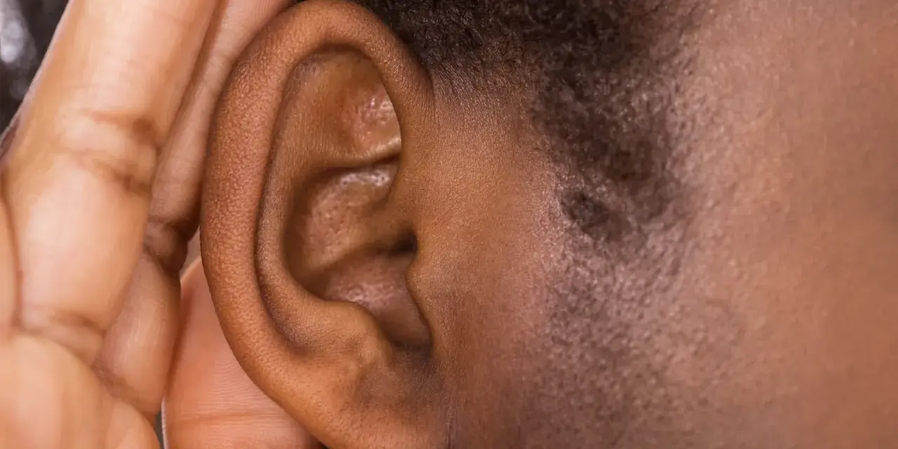 Une main couvre une oreille, comme pour mieux entendre ou se protéger du bruit. Cela peut évoquer ce qu'est-ce qui provoque des acouphènes.