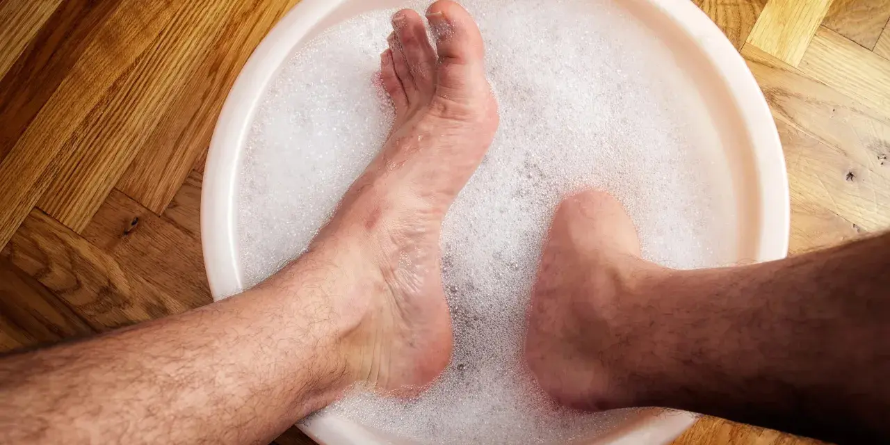 A person's feet soaking in a bubbly foot bath on a wooden floor.