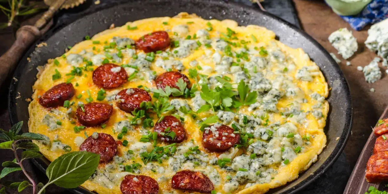 Pyszny omlet na słono z kawałkami chorizo i niebieskim serem, posypany szczypiorkiem i natką pietruszki.