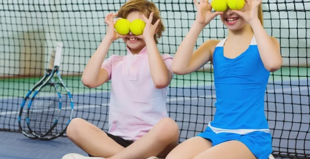 Bambini che fanno sport, con palline da tennis sugli occhi, ridono su un campo da tennis.