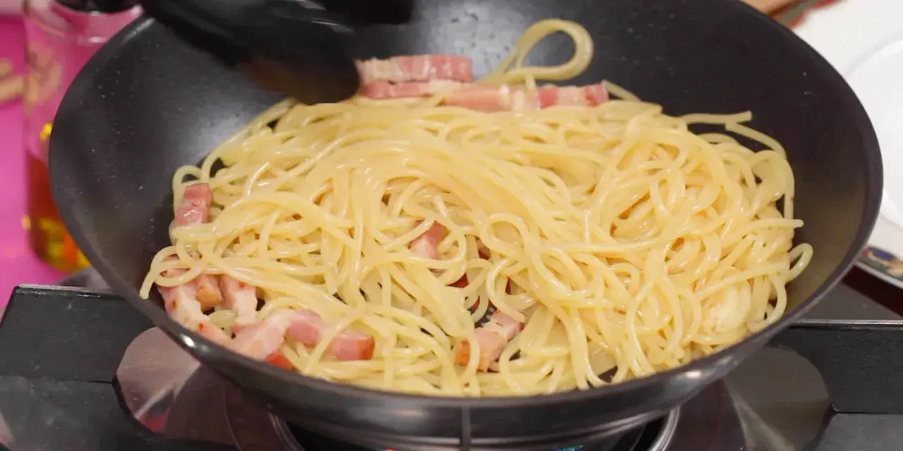 Espaguetis con trozos de panceta en una sartén, preparándose para unos deliciosos tallarines a la carbonara.