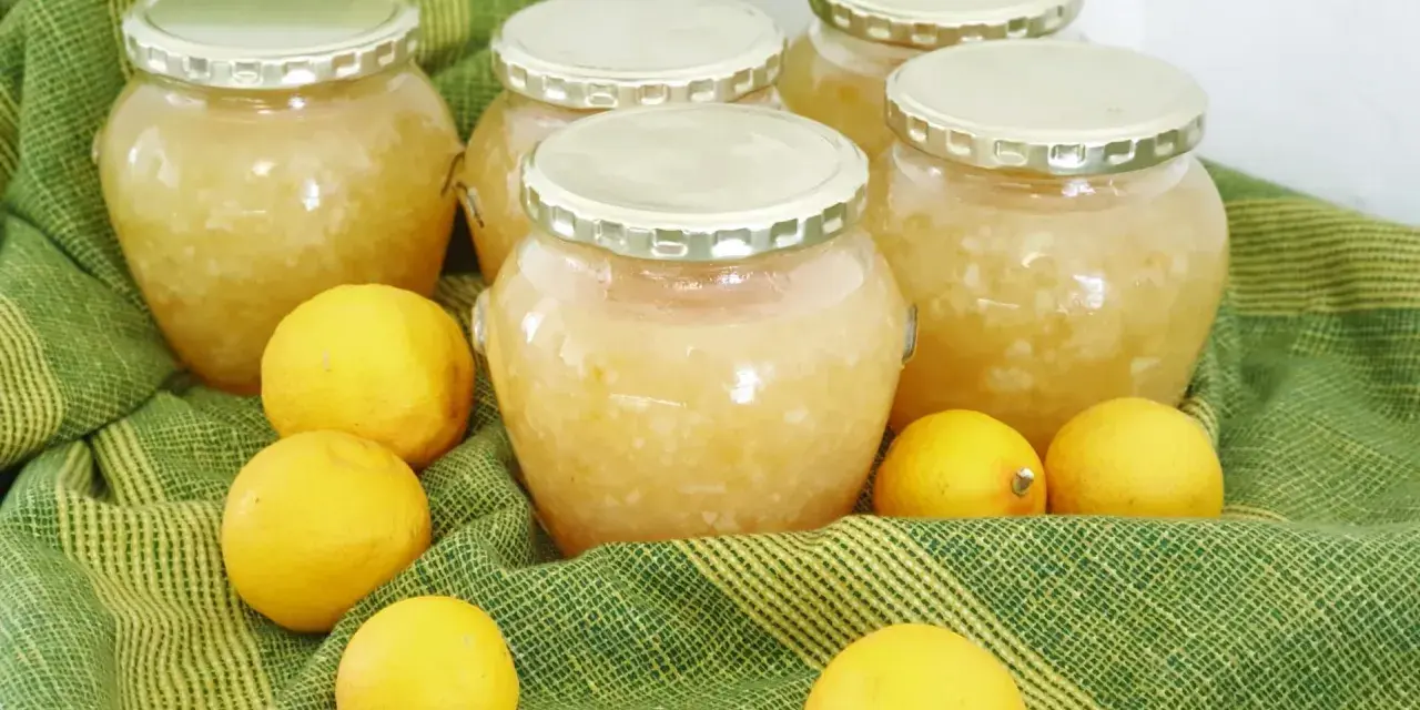 Plusieurs bocaux de confiture de citron maison, entourés de citrons frais, sur un tissu vert rayé.