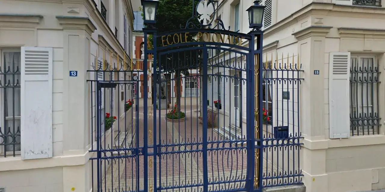 Brama do Ecole de Paris, ozdobiona złotymi detalami, prowadzi na dziedziniec z drzewem i ławką.
