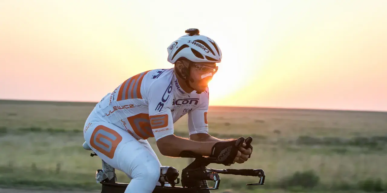 Cyclist in aerodynamic gear races across America at sunset, pushing through the vast landscape.