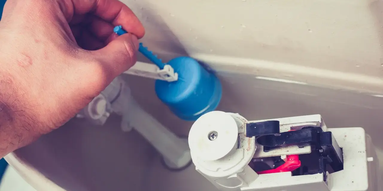 Dłoń demontuje niebieski pływak, pokazując mechanizm, jak wyjąć zawór spustowy Cersanit.