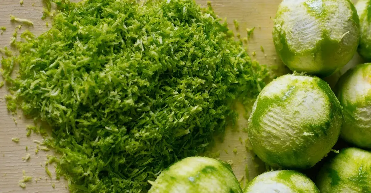 Świeżo starta skórka z limonki, idealna do kordiałów, leży obok kilku obranych owoców.