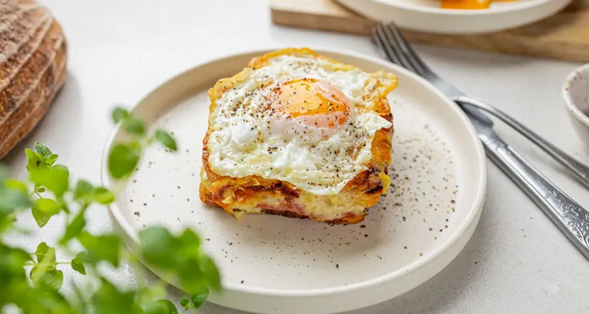 Pyszny croque madame z jajkiem sadzonym na wierzchu, podany na talerzu z pieprzem i ziołami.