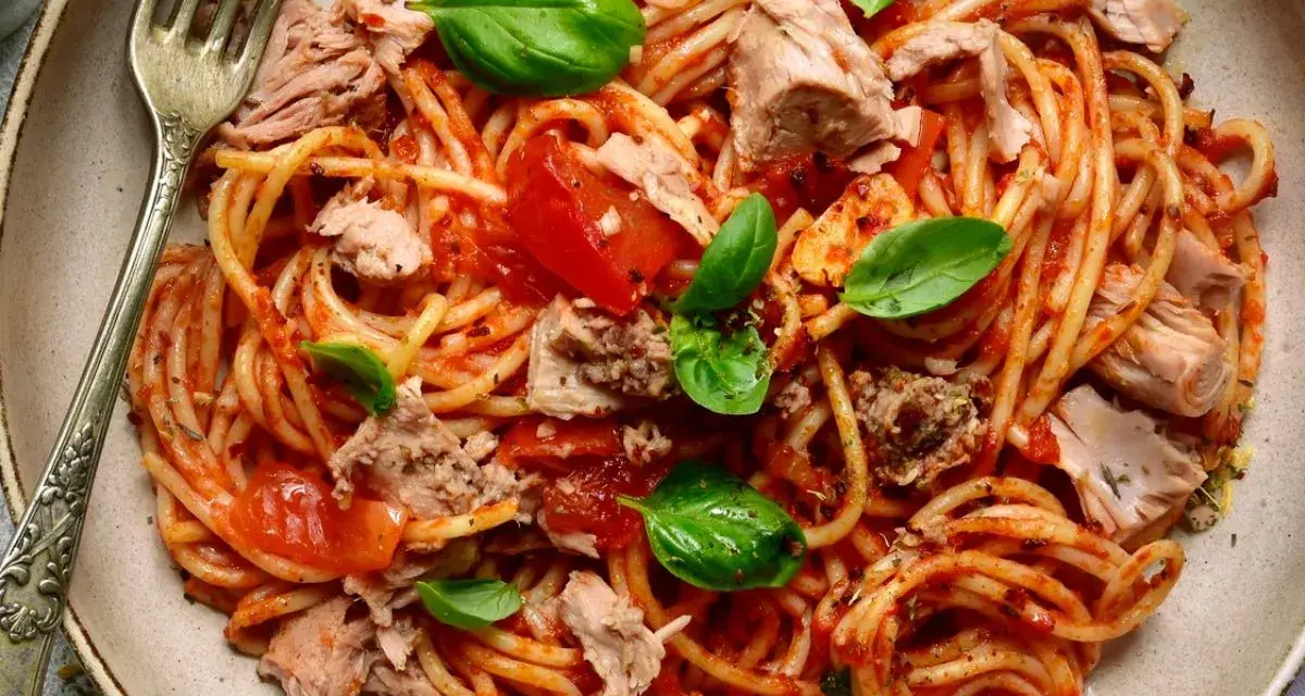 Spaghetti al sugo di pomodoro con abbondante tonno in scatola, guarniti con foglie di basilico fresco. Un piatto semplice e gustoso.