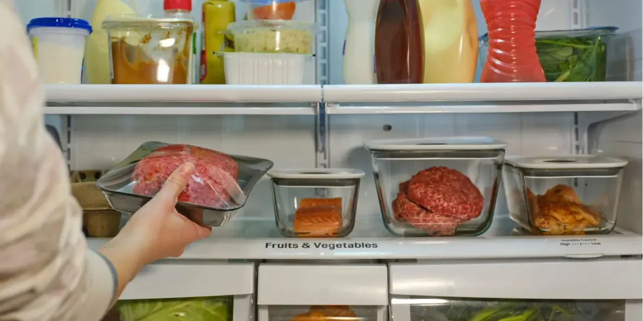 Mano colocando carne picada envasada en un refrigerador lleno de alimentos.
