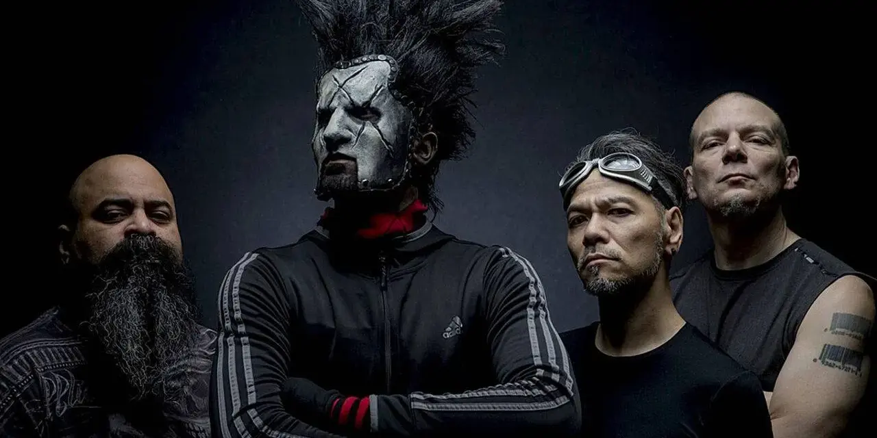 Quatre hommes, dont un avec un maquillage facial blanc et une crête, posent pour une photo. Le groupe Static X semble prêt à monter sur scène.