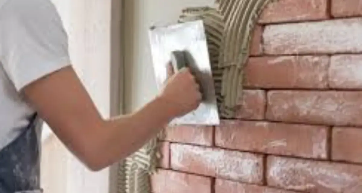 Un ouvrier applique de l'enduit sur une brique avec une truelle, créant une texture rustique.