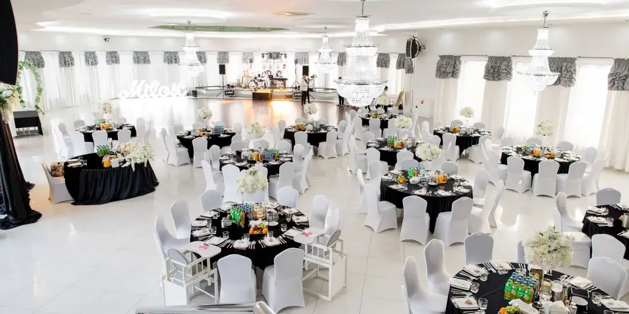 Elegancka sala weselna z czarnymi obrusami i białymi pokrowcami na krzesła. Stoły zastawione, gotowe na przyjęcie gości. Zastanawiasz się, ile za talerzyk na weselu?