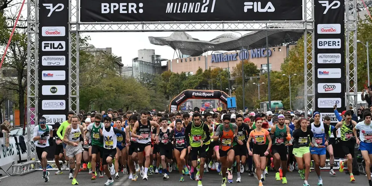 Corredores listos para la media maratón Milán 2021. La carrera arranca bajo un arco con patrocinadores y el logo de Fila.