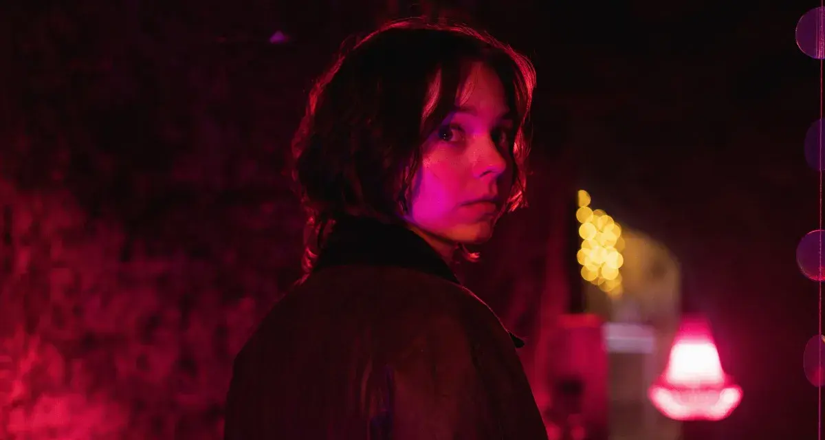 Młoda kobieta z zaciekawieniem spogląda przez ramię w mrocznym, neonowym otoczeniu. Czy to scena z nowego serialu Netflix?