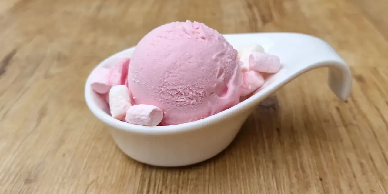 Eine Kugel rosa Bubble Gum Eiscreme mit Marshmallows in einer weißen Schale auf Holzhintergrund.