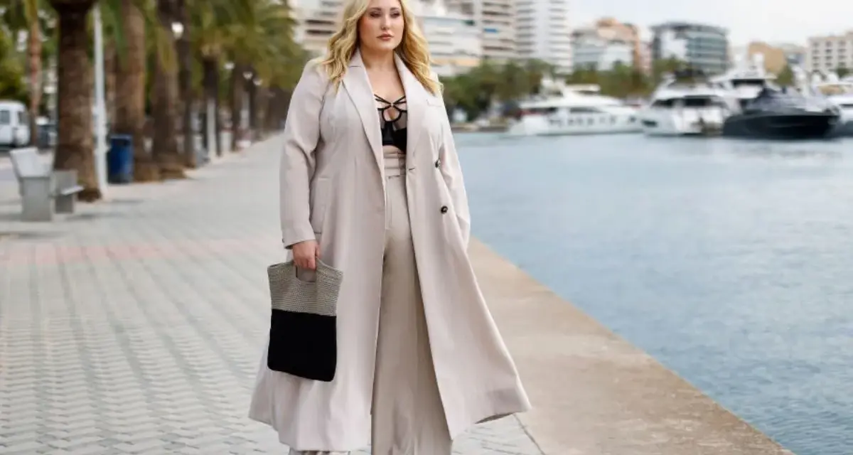 Kobieta o figurze jabłko w eleganckich stylizacjach, z torebką, na tle palem i jachtów.