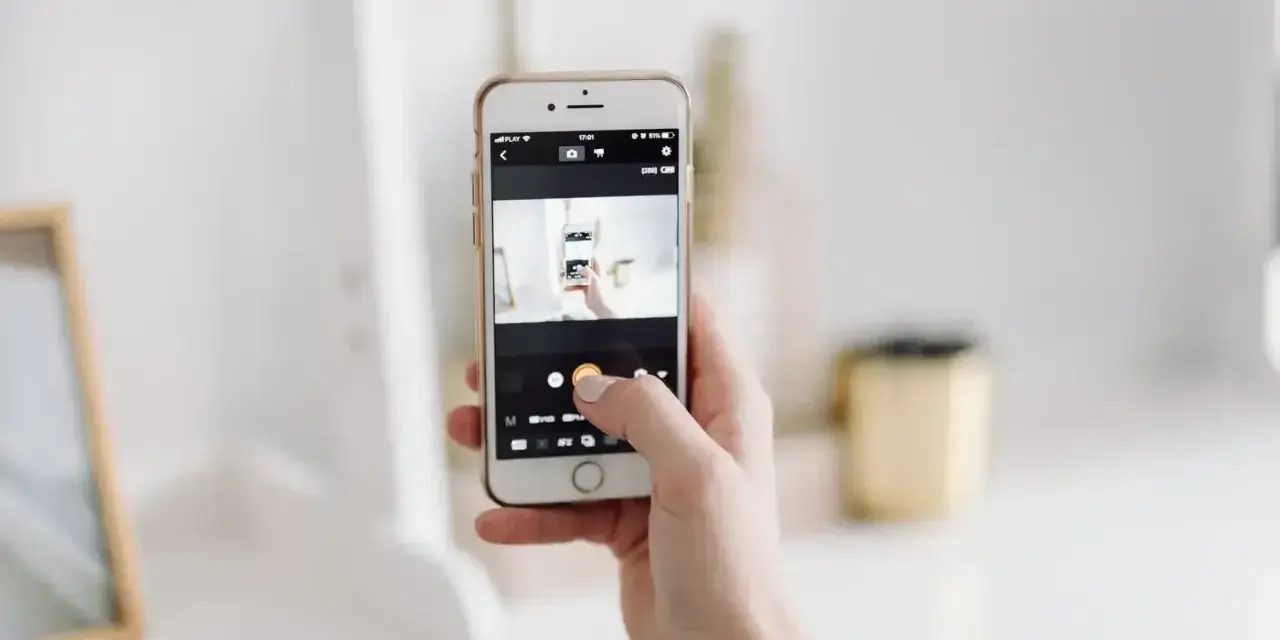 Dłoń trzyma smartfon, na ekranie którego widać aplikację do robienia zdjęć. To jakby snapbridge po polsku, ułatwiający dzielenie się wspomnieniami.