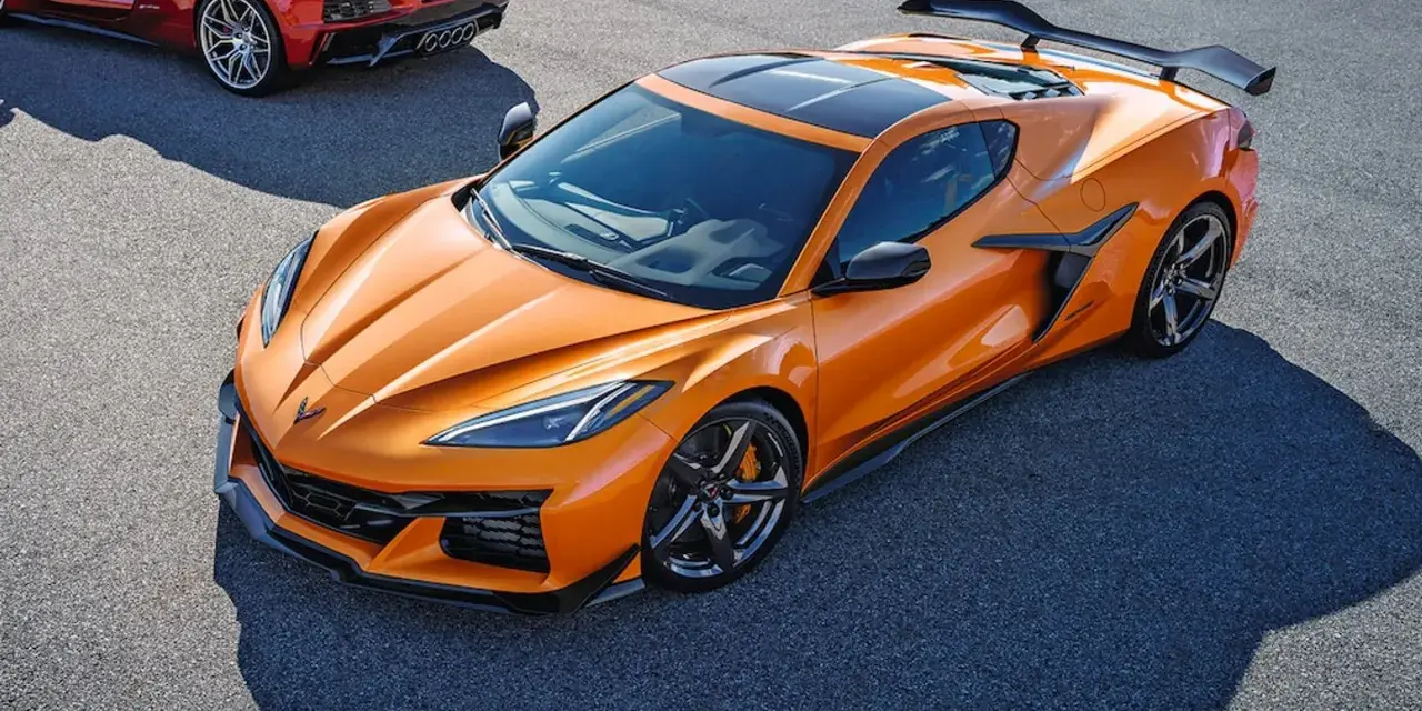 Pomarańczowy Chevrolet Corvette C8 z czarnym dachem i spojlerem na torze wyścigowym. Obok widać fragment czerwonego samochodu.