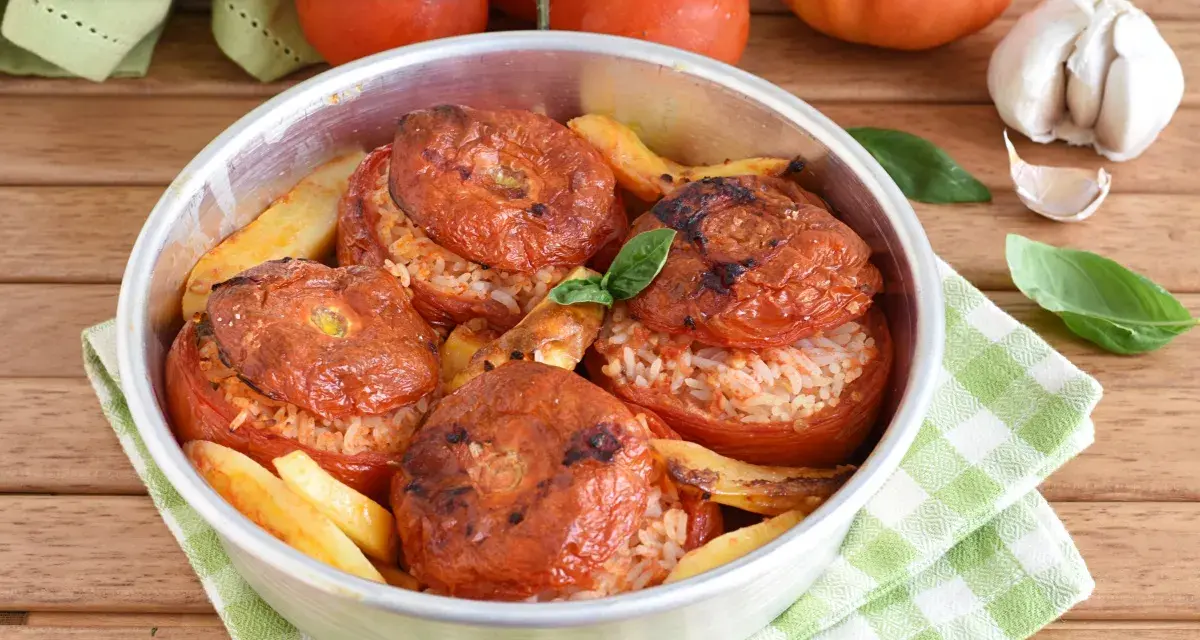 Pomodori ripieni di riso, cotti al forno con patate e basilico. Un piatto estivo saporito e colorato.