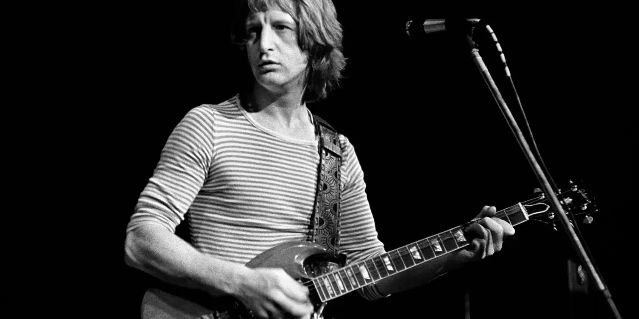 Pete Ham, mit gestreiftem Shirt und Gitarre, blickt konzentriert auf die Bühne.