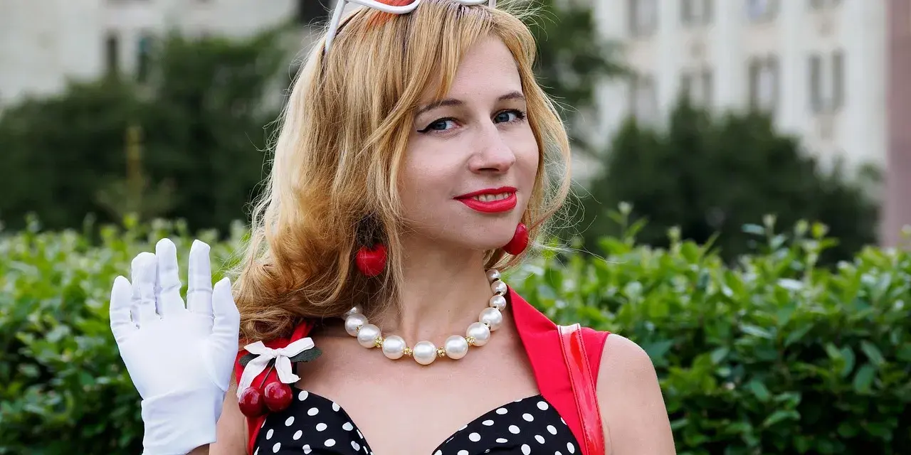 Una mujer con guantes blancos saluda, luciendo un vestido de lunares y cerezas. ¡Buenos días, señorita en francés!